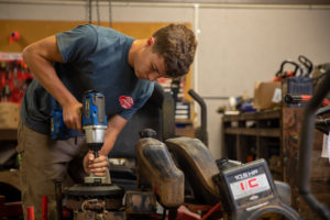 Man using a power tool on a riding lawn mower inside the repair shop