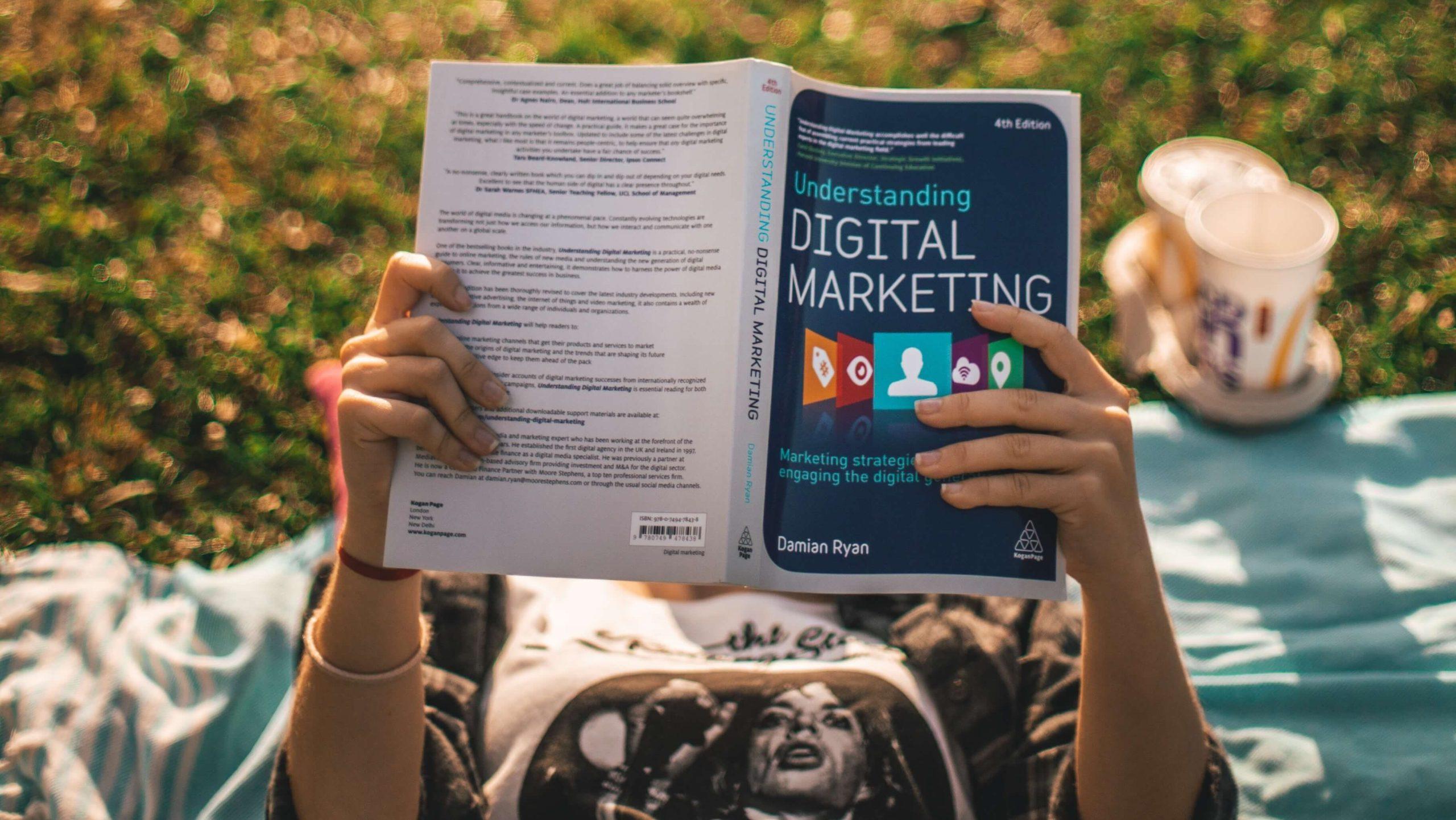 girl laying on ground, reading digital marketing book